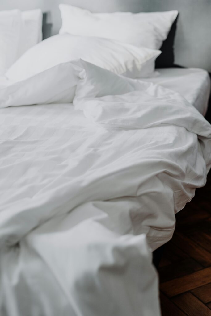 Soft white bamboo sheets and pillows on an elegant bed with dark wood flooring